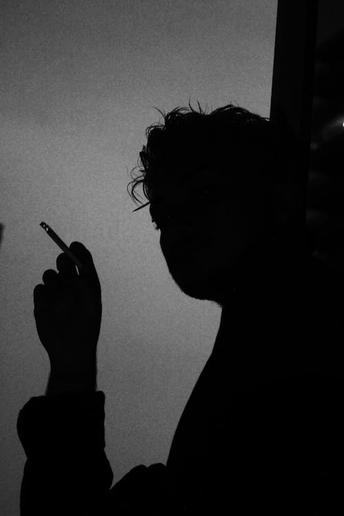Free Black and white low angle side view of silhouette of person smoking cigarette while resting alone and thinking on problem Stock Photo