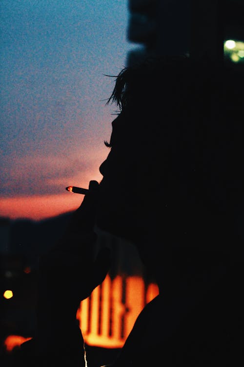 Calm person with burning cigarette smoking in dark evening