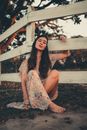 Woman Sitting on the Ground Barefoot in a Summer Dress Holding a Wooden Fence