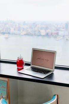 A laptop with motivational text and a drink placed on a windowsill overlooking the New York City skyline.