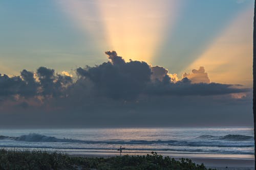Free Sun Rays Visible From Behind the Clouds Above a Sea  Stock Photo
