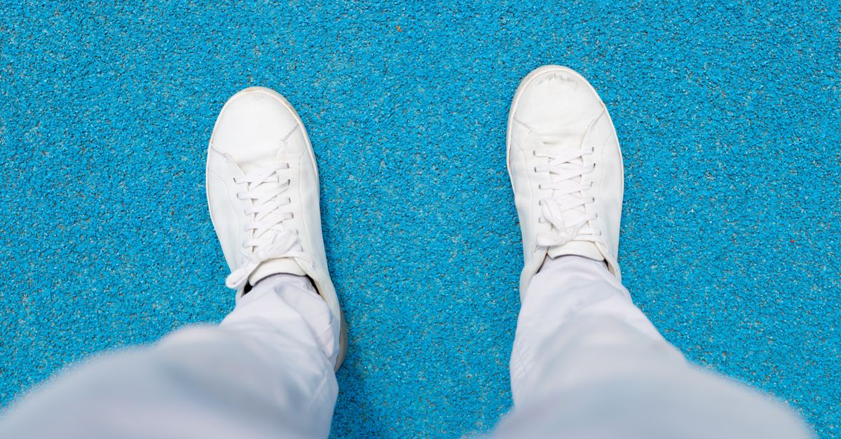 White sneakers paired with sweatpants on a vibrant blue surface, viewed from above.