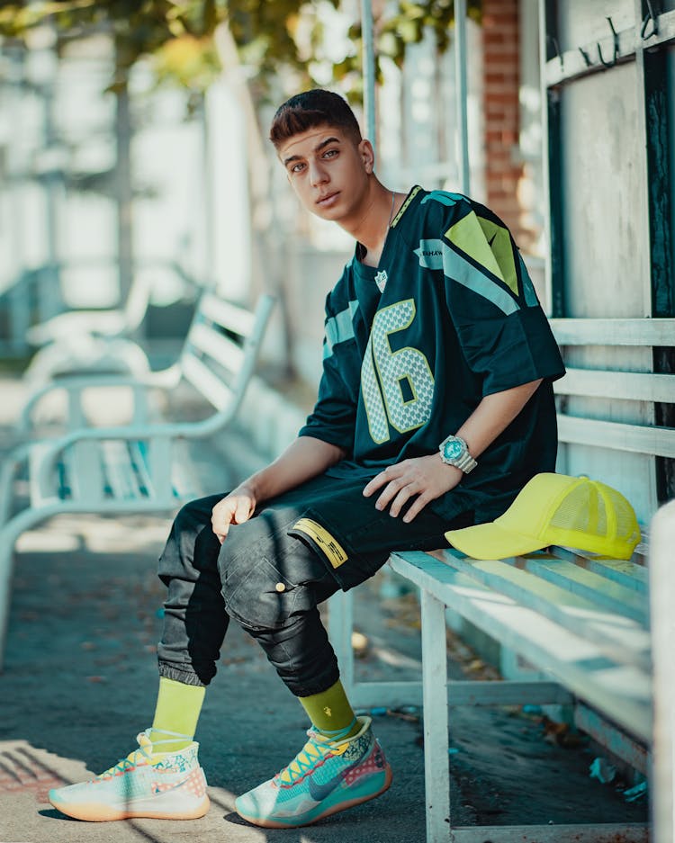 Young Man Sitting On A Bench In City Wearing A Football Jersey 