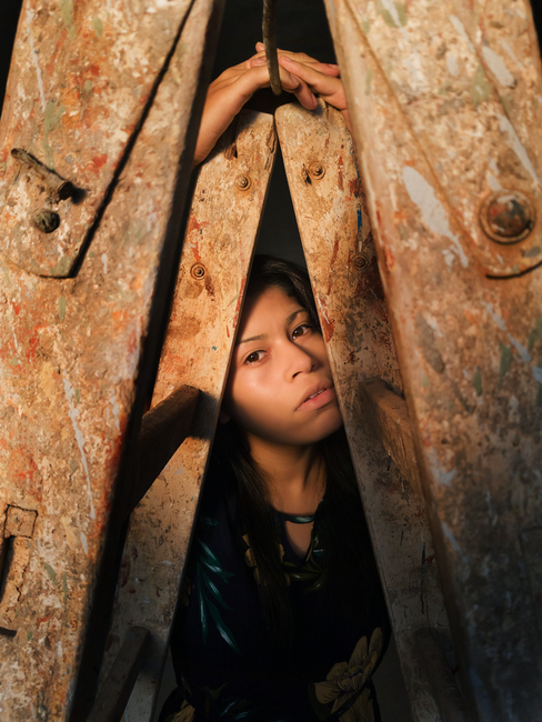 A creative portrait of a woman peering through a rusted trestle ladder, creating an artistic frame.