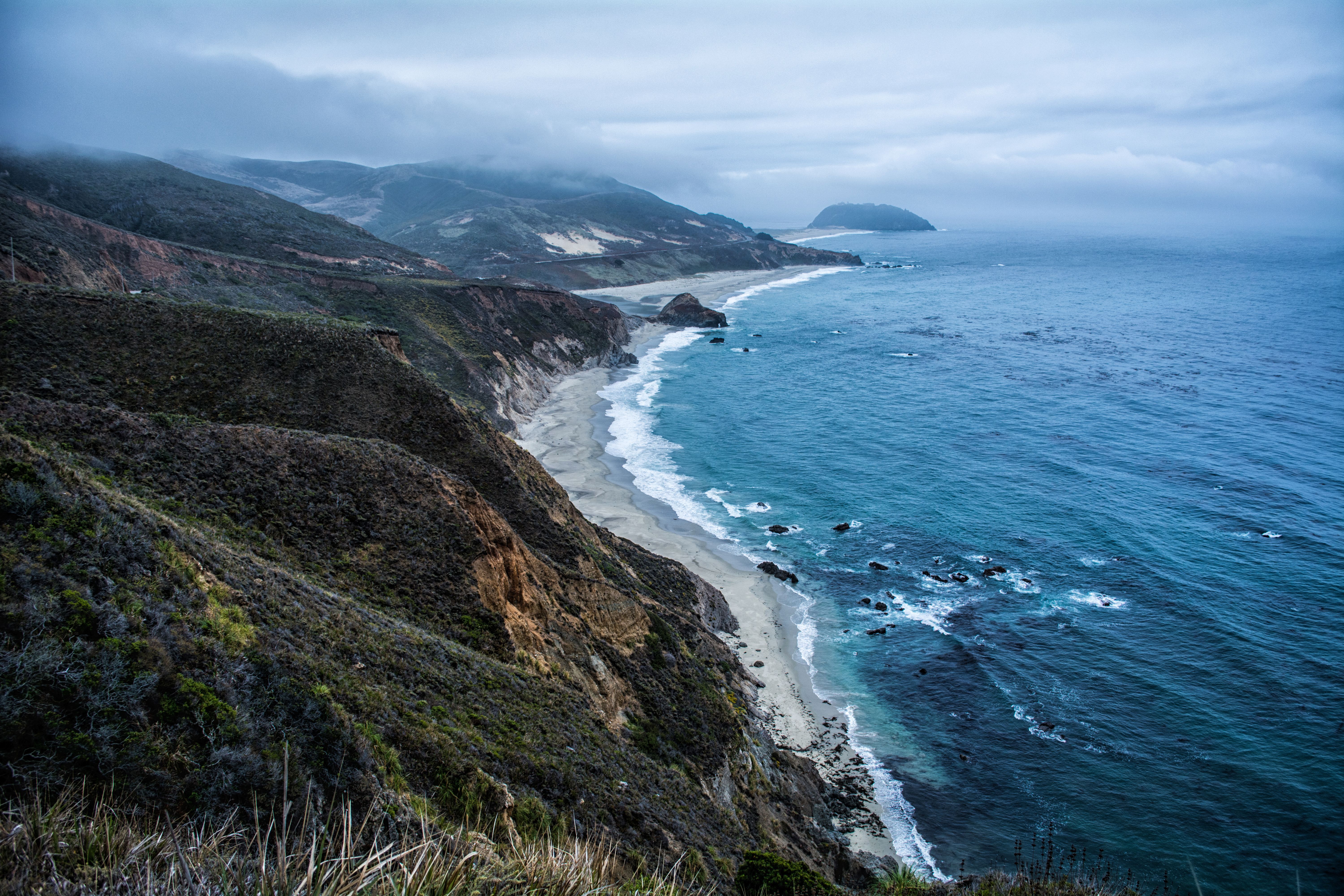 Scenic view of a rugged coastline with waves crashing against the shore under a cloudy sky.