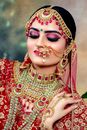 Beautiful Indian bride in traditional wedding red sari with golden embroidery heavy jewellery and bright make up