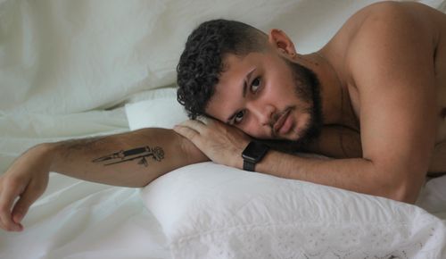Free A bearded man with a tattoo reclines comfortably on white pillows, exuding serenity and style. Stock Photo