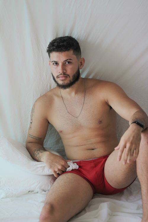 Free A confident young man poses shirtless in red swimwear on a white background. Stock Photo