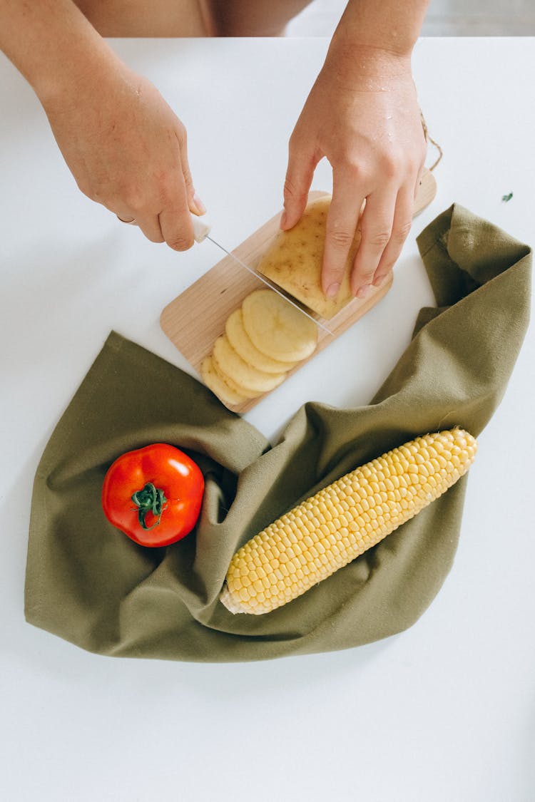 A Person Slicing Potato On A Wooden Chopping Board