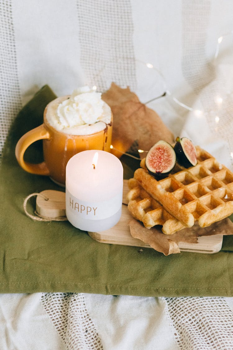 A Candle On Chopping Board With Waffles Beside A Mug With Creamy Drink