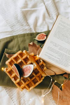 Warm waffles topped with fresh figs, set on a textured cloth alongside an open book in a cozy autumn setting.