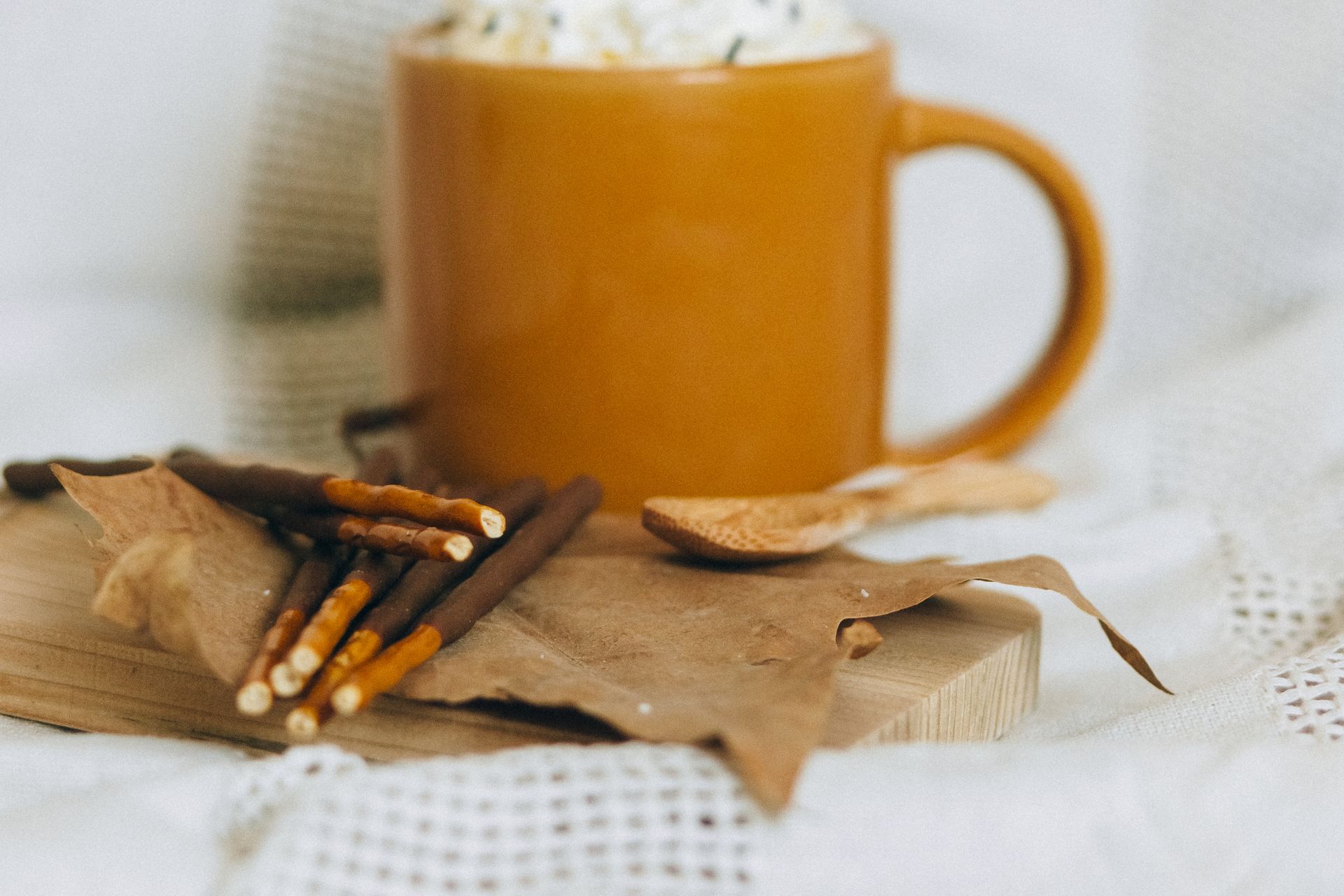 Warm mug of hot chocolate with pretzels, maple leaf, and wooden spoon on a cozy autumn setting.