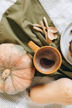Warm autumn-themed flat lay featuring a coffee cup, pumpkins, and wooden spoons.