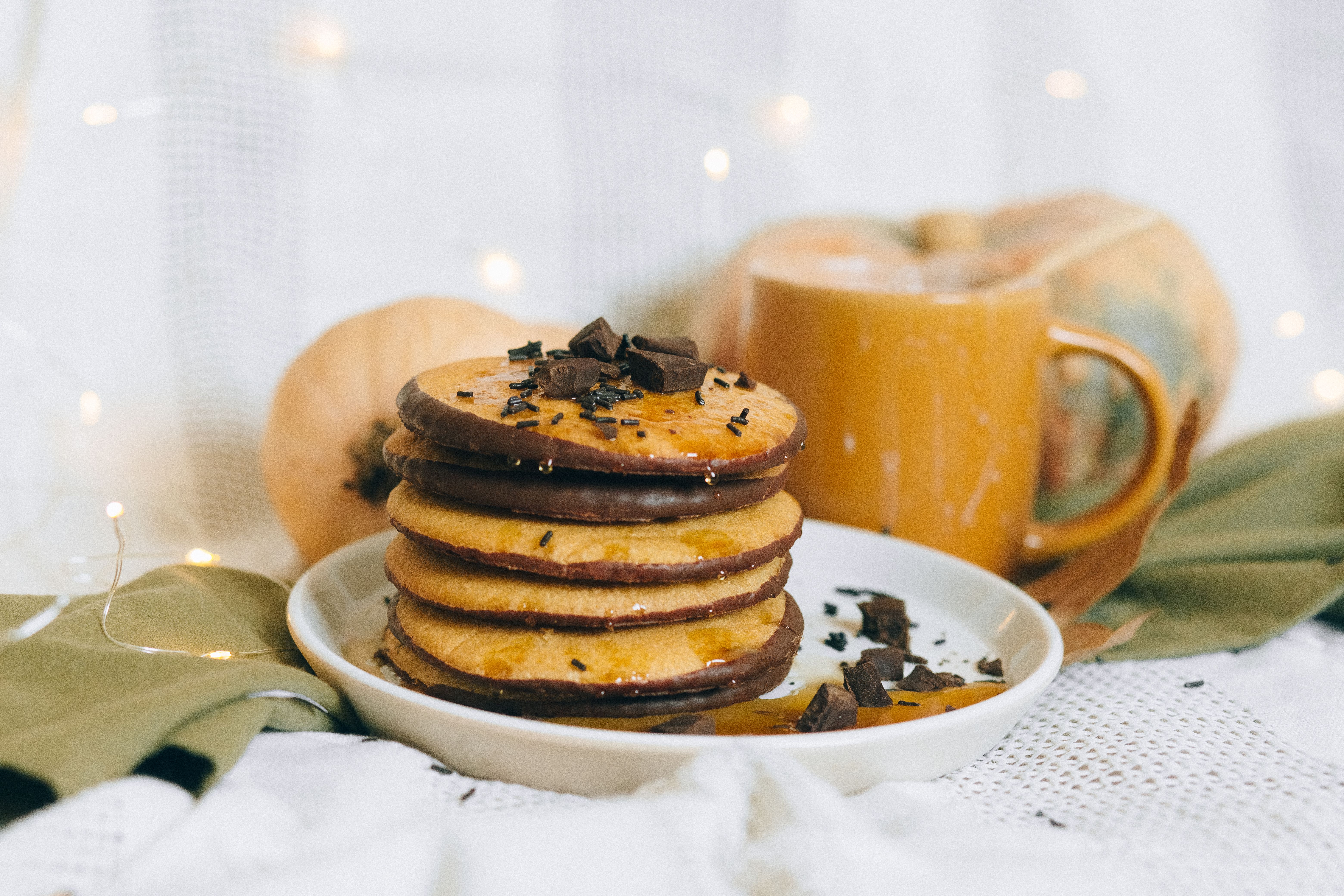 Stack of pumpkin pancakes with chocolate, fall decor, and warm drink.