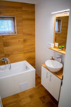 Interior of stylish bathroom with wooden floor and wall with sink under mirror and bath