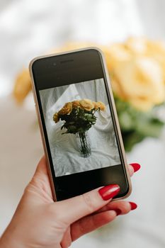 Close-up of a smartphone capturing a vase with yellow roses. Ideal for floral and technology themes.