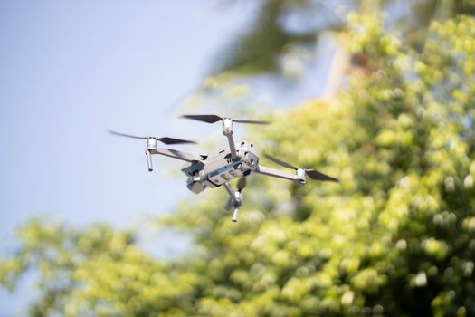 A close-up shot of a drone flying outdoors against a clear sky and green foliage.