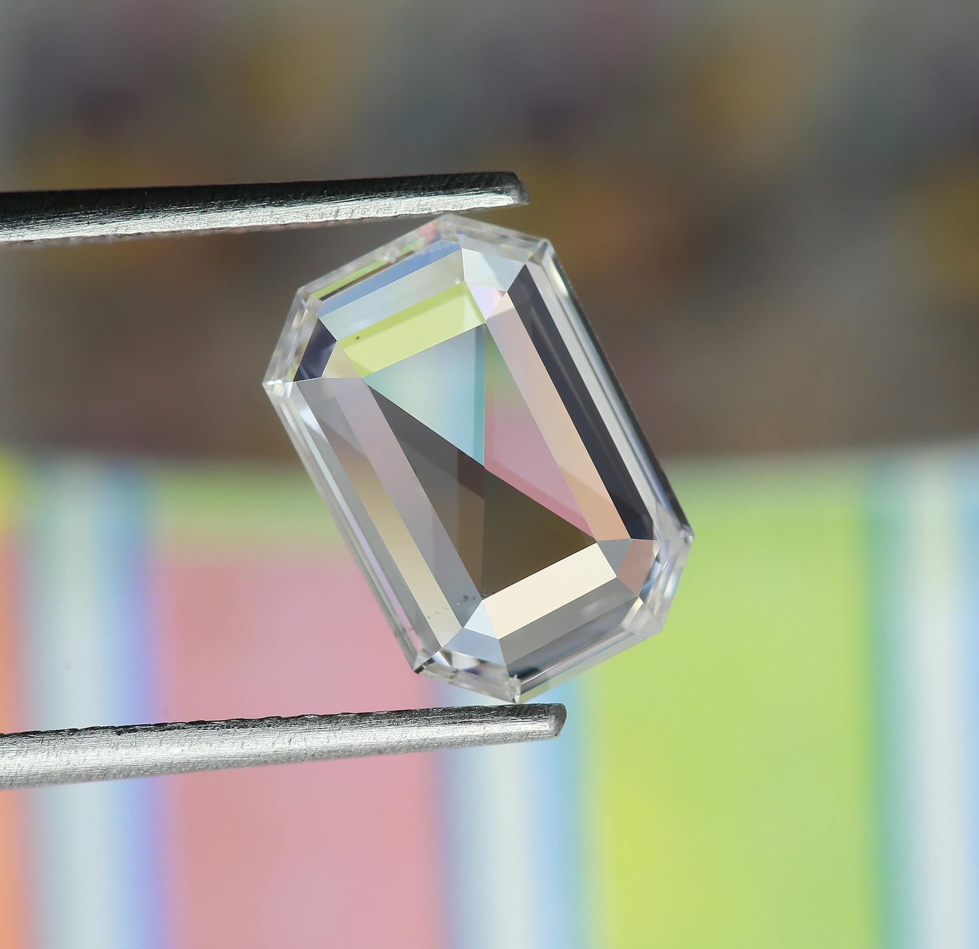 Close-up of a stunning emerald cut diamond held by tweezers, perfect for luxury designs.