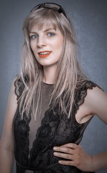Chic studio portrait of a blonde woman wearing black lace against a gray background, exuding elegance.