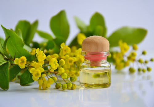 Yellow Flowers Beside a Clear Glass Bottle with Essential Oil