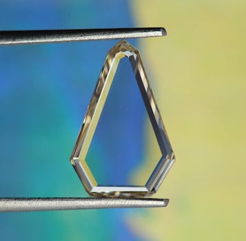 Detailed close-up view of a transparent crystal held by metallic tweezers, showcasing geometric design and luxury appeal.