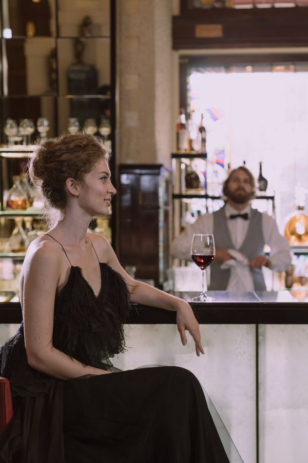 Woman in a black evening dress enjoying wine at a luxurious bar
