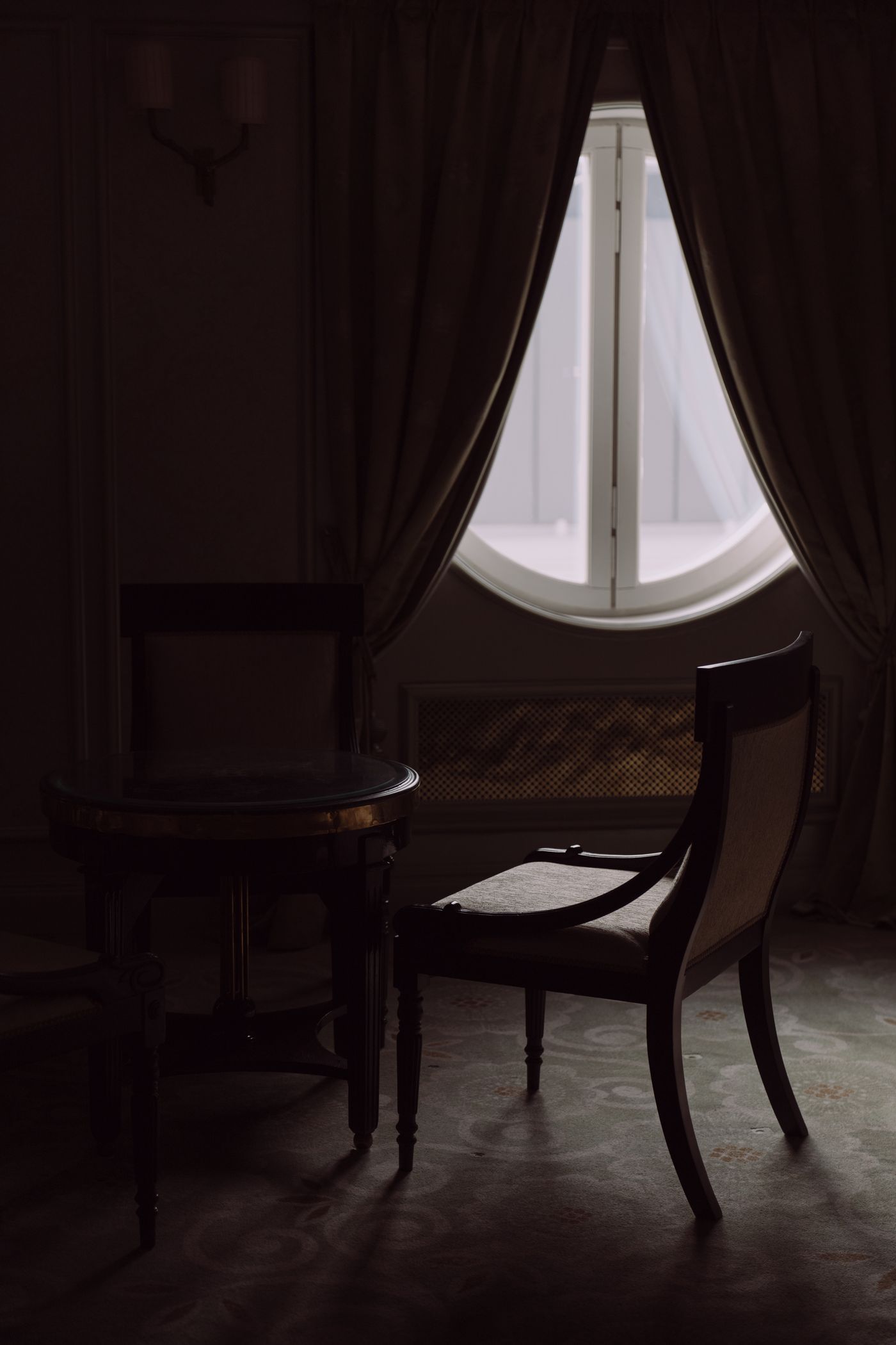 A quiet interior with a large arched window and wooden chairs