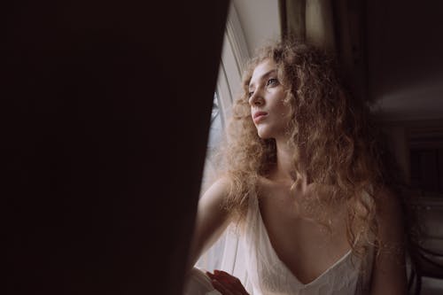 Woman in White Sleeveless Dress Looking Out a Window