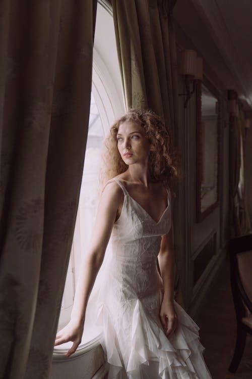 Woman in White Dress Standing Beside Window
