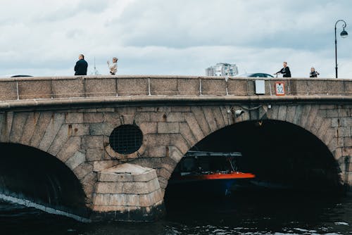 Tourists on big bridge over small passenger ship sailing on river in daytime