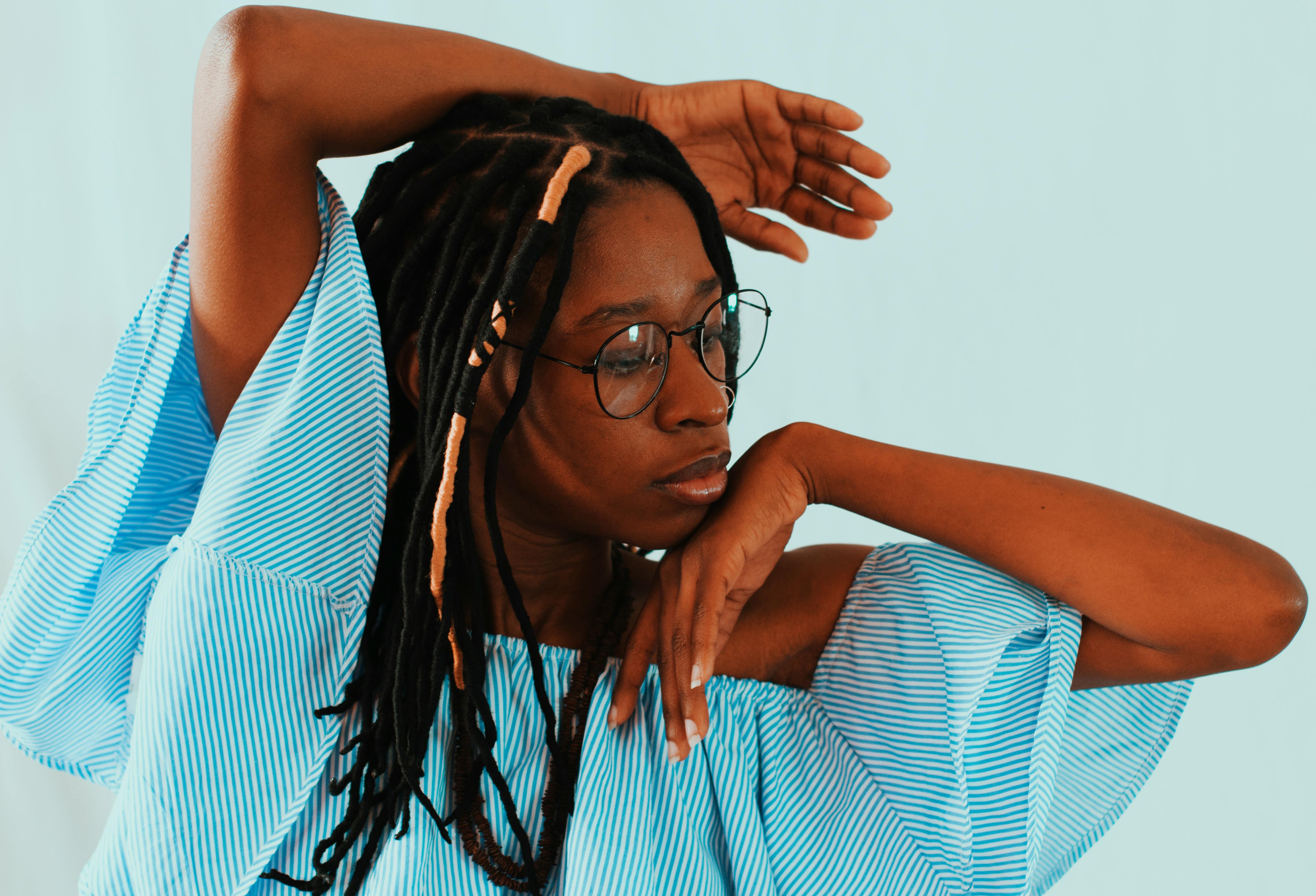 Elegant portrait of a woman in glasses and dreadlocks posed against a light blue backdrop.