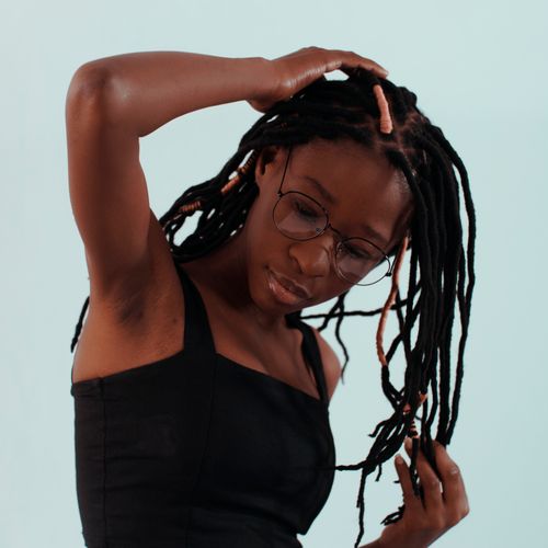 Free Studio portrait of a woman with dreadlocks and eyeglasses, captured in a stylish black outfit against a light blue background. Stock Photo