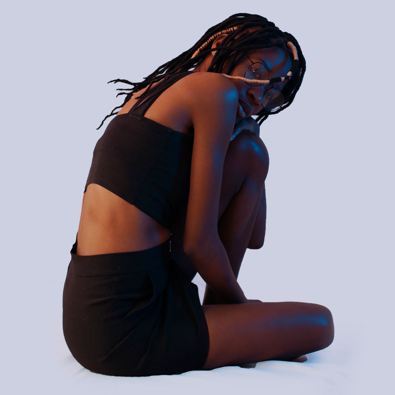 Artistic studio portrait of a woman with dreadlocks and eyeglasses posing elegantly.