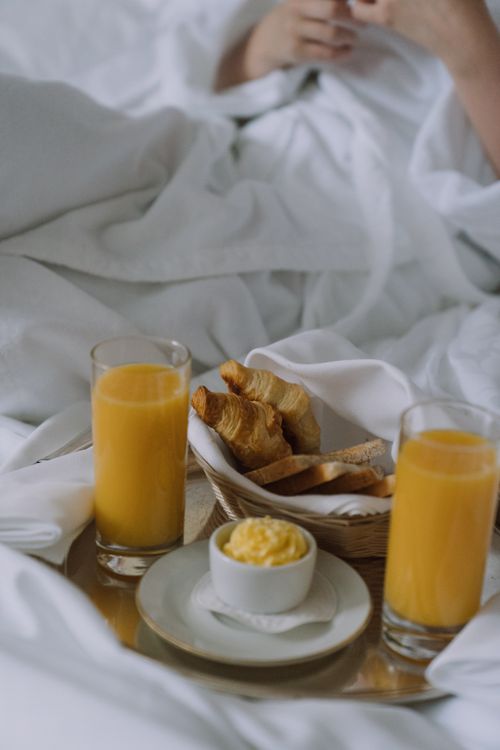 Free Cozy breakfast in bed featuring croissants, orange juice, and butter for a relaxing morning meal. Stock Photo
