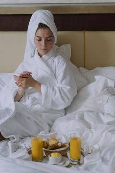 一位穿着浴衣的女士正在床上享用早餐，早餐有橙汁和糕点