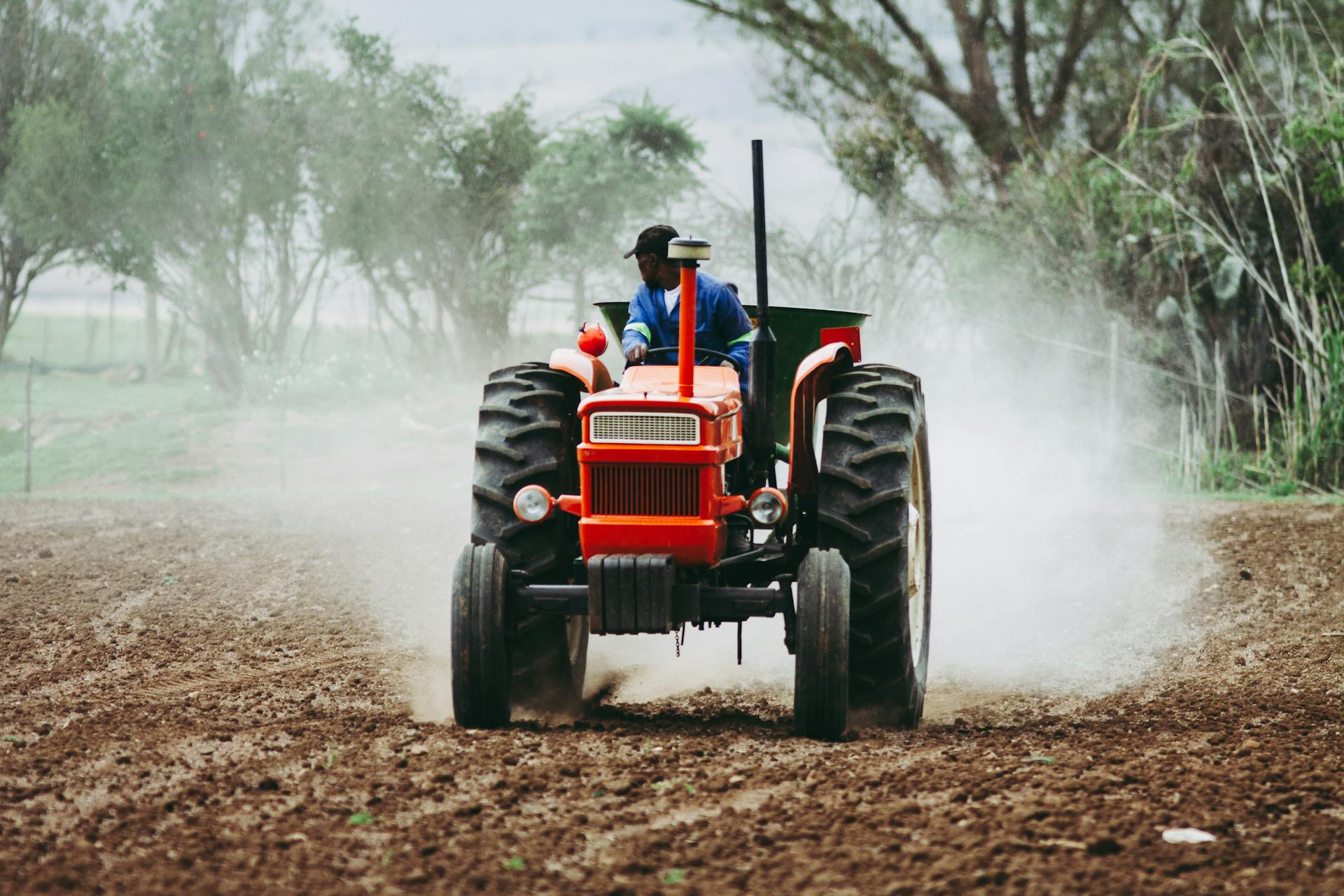 A man rides a red tractor while plowing a dusty field, showcasing agriculture and farming equipment.