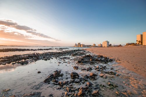 Free Serene sunset over a rocky beach with a distant coastal city skyline. Stock Photo