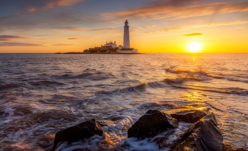 Free Scenic view of a lighthouse during sunrise with ocean waves and rocky shore. Stock Photo