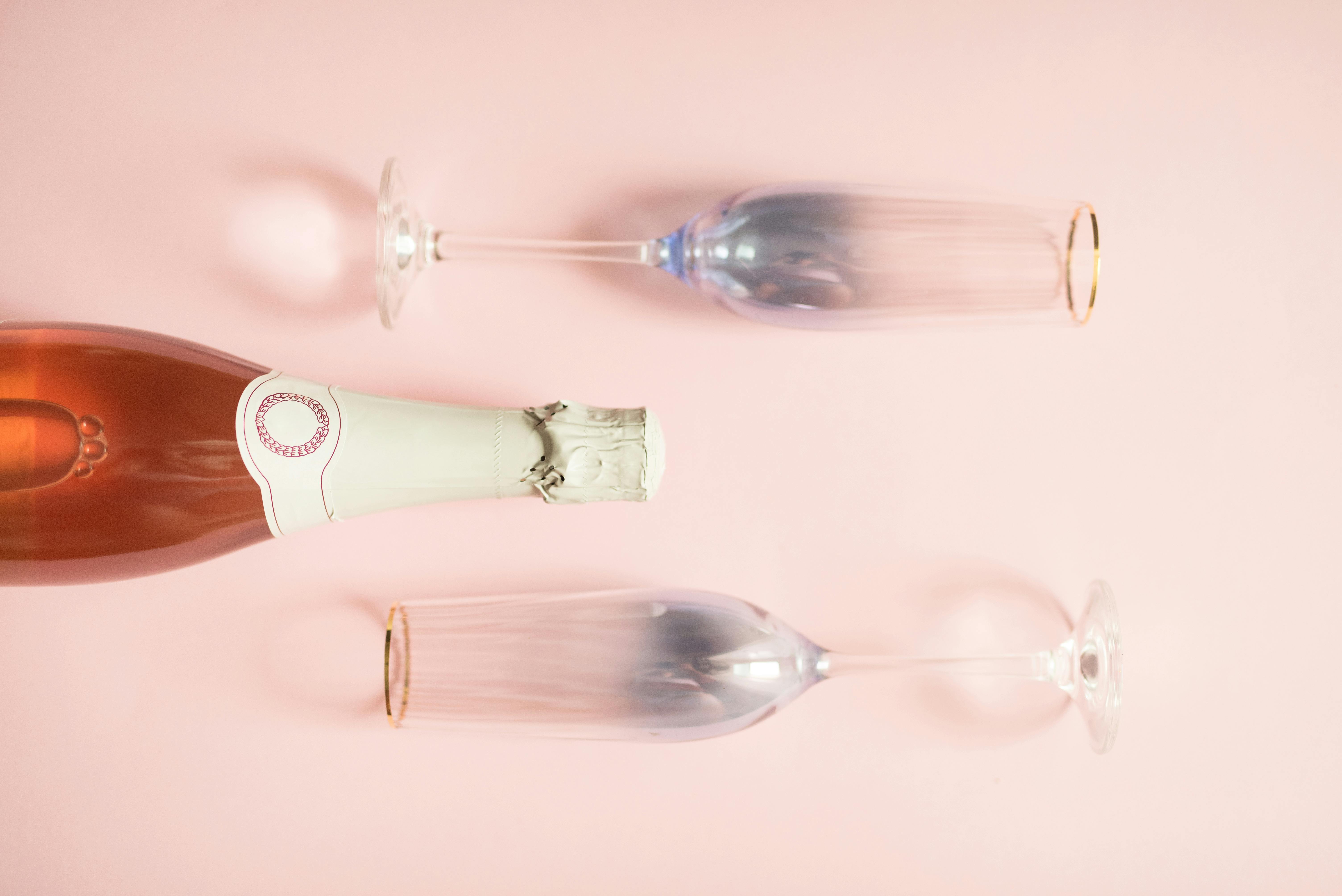 粉红色背景前，香槟瓶与两个玻璃杯风格优雅，非常适合庆祝活动和聚会