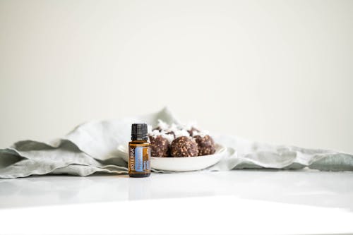 Free Brown Glass Bottle with Essential Oil Beside a Small Plate of Chocolate Goodies Stock Photo