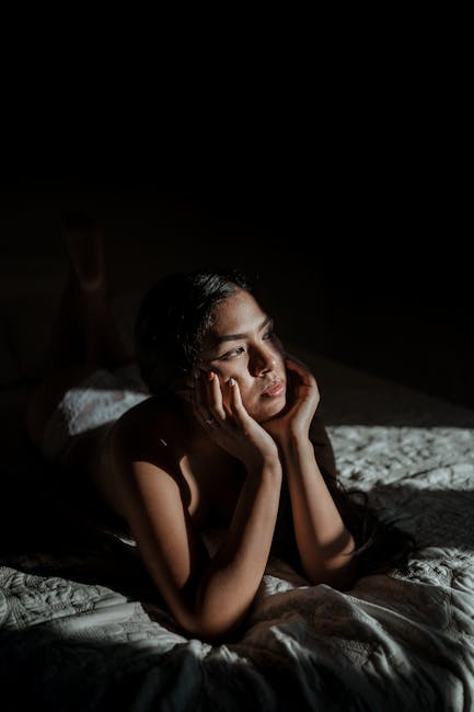 A contemplative woman lounges on a bed, bathed in dramatic sunlight, evoking introspection.