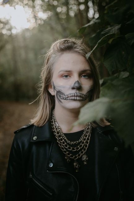A young woman with skull face paint and leather jacket in a forest, perfect for Halloween.