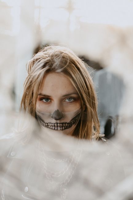 Attractive female with skull face art looking at camera through chain link fence