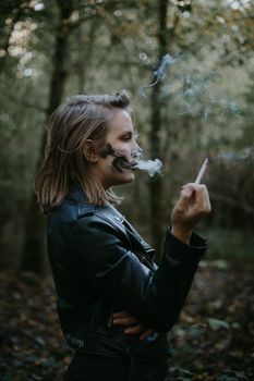 一名女子涂着骷髅脸彩绘，在森林中侧身吸烟，营造出万圣节的氛围