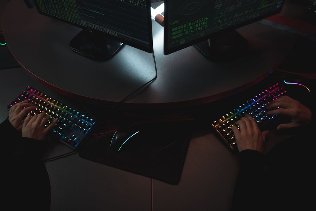 Due persone digitano su tastiere RGB davanti a schermi pieni di codice in un contesto di cybersicurezza, scenario tipico di un team SOC