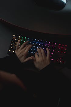 A person typing on a colorful backlit mechanical keyboard in a dark setting.