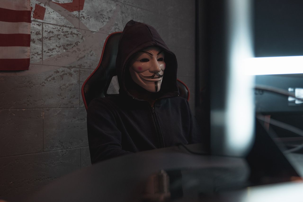 a mysterious person in a guy fawkes mask working at a computer symboli