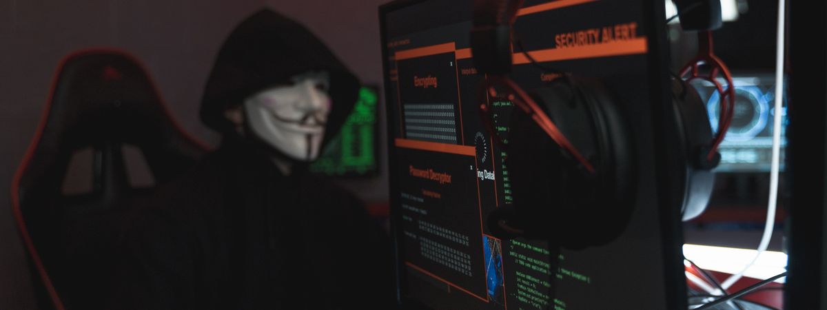 Persona encapuchada frente a un ordenador en una habitación oscura