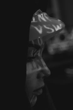 Artistic black and white close-up of an anonymous hacker with projected text, highlighting cyber security themes.