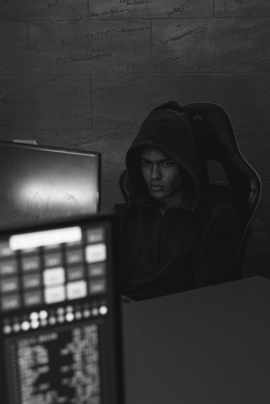 Een serieuze hacker in een donkere kamer, gefocust op een computerscherm, belichaamt cyberbeveiligingsbedreigingen.